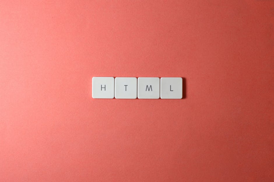 A close-up image featuring four white square tiles with black letters positioned on a pink surface. The tiles are arranged in a straight line and spell out the word 'HTML'. The surface appears to be s
